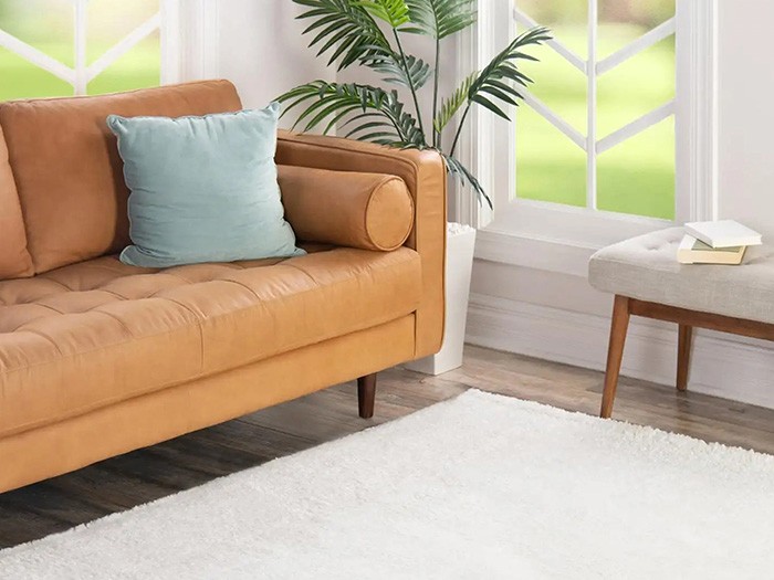 White area rug covering wood floors next to a sofa and windows.